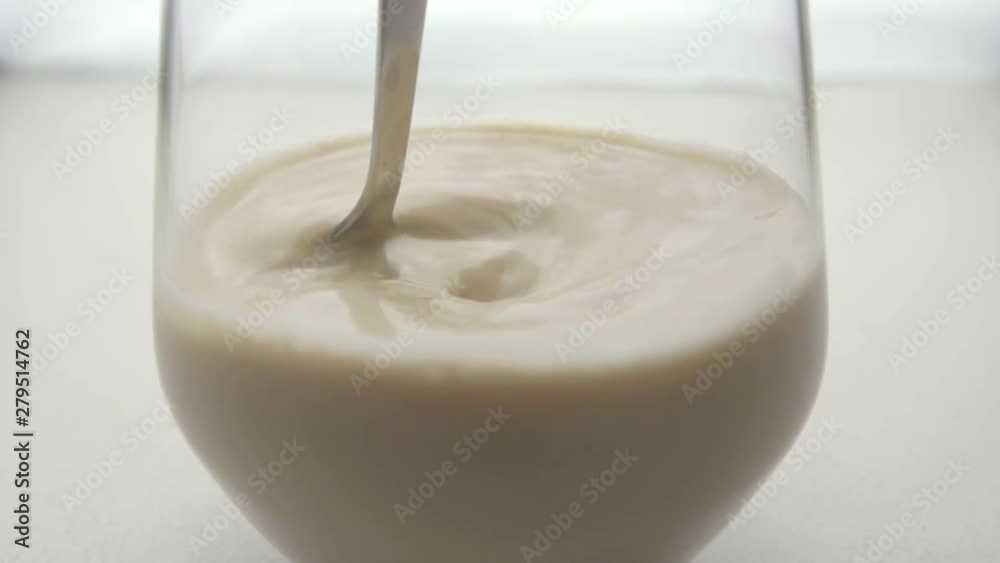 Coffee in glass mixing with metallic spoon. White background. Slow motion. Close-up. Coffee in glass mixing with metallic spoon. White background. Slow motion. Close-up.