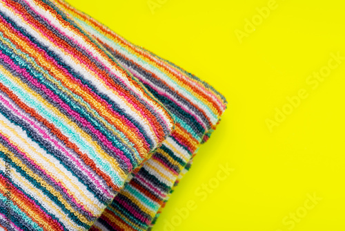 Folded Colorful Striped Organic Cotton Beach Towels on bright yellow background.