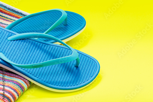 Folded Colorful Striped Organic Cotton Beach Towels and Blue Flip Flops on bright yellow background.