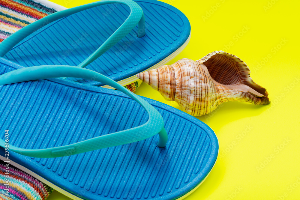 Folded Colorful Striped Organic Cotton Beach Towels, Blue Flip Flops and Sea Shell on bright yellow background.