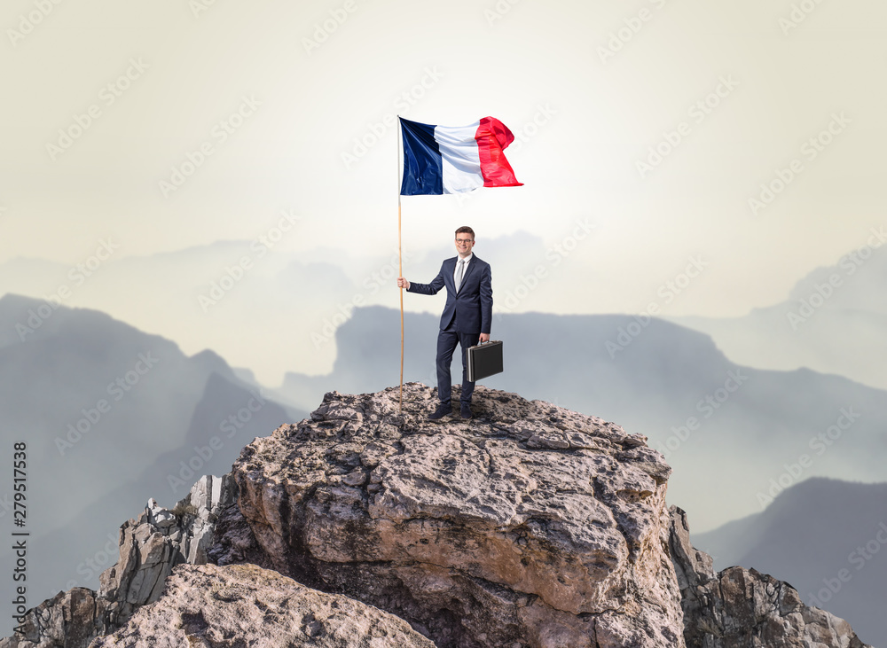 Obraz premium Successful businessman on the top of a mountain holding France victory flag