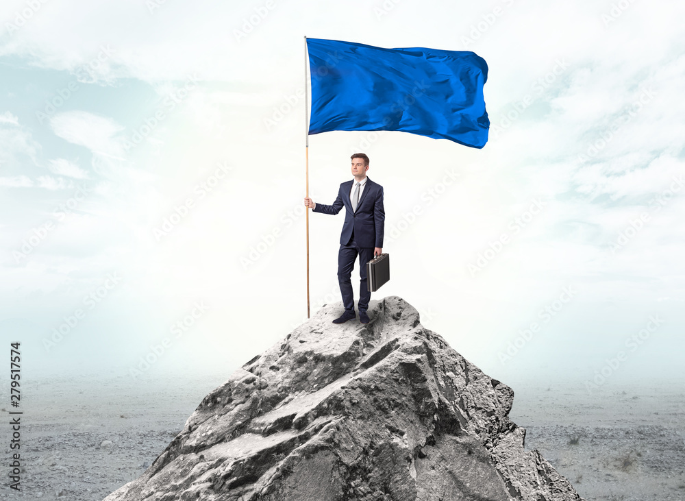 Obraz premium Handsome businessman on the top of the mountain with blue flag