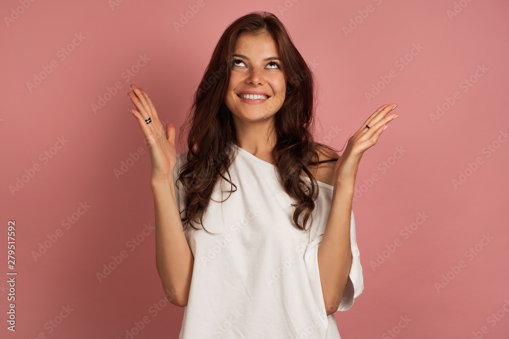 Young brunette looks up spreading her hands with a smile, pink background Young brunette looks up spreading her hands with a smile, pink background