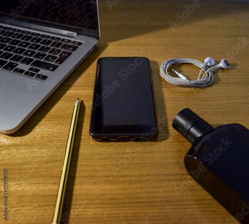 Vista de un teléfono inteligente con un ordenador, auriculares, lápiz y perfume en mesa de madera