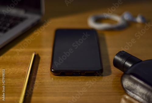 Vista de un teléfono inteligente con un ordenador, auriculares, lápiz y perfume en mesa de madera