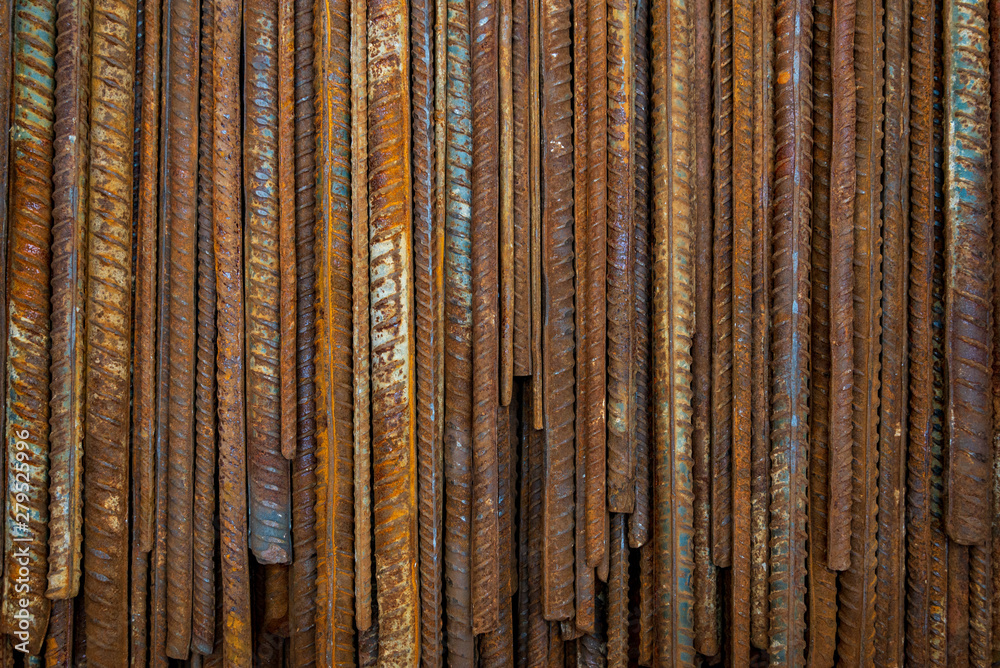 Fototapeta premium Top view stack of straight old rusty high yield stress deformed reinforcement steel or iron bars. Background vertical random pattern of deformed iron bars. 