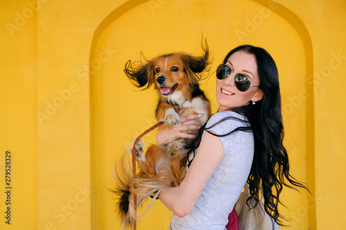 Fotografi Portrait of Brunette woman and her dog on background of bright yellow wall