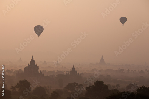 Orange mystical sunrise landscape view with silhouettes of old ancient temples and palm trees in dawn fog from balloon, Bagan, Myanmar. Burma