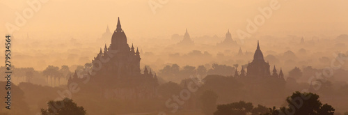 Orange mystical sunrise landscape view with silhouettes of old ancient temples and palm trees in dawn fog from balloon, Bagan, Myanmar. Burma