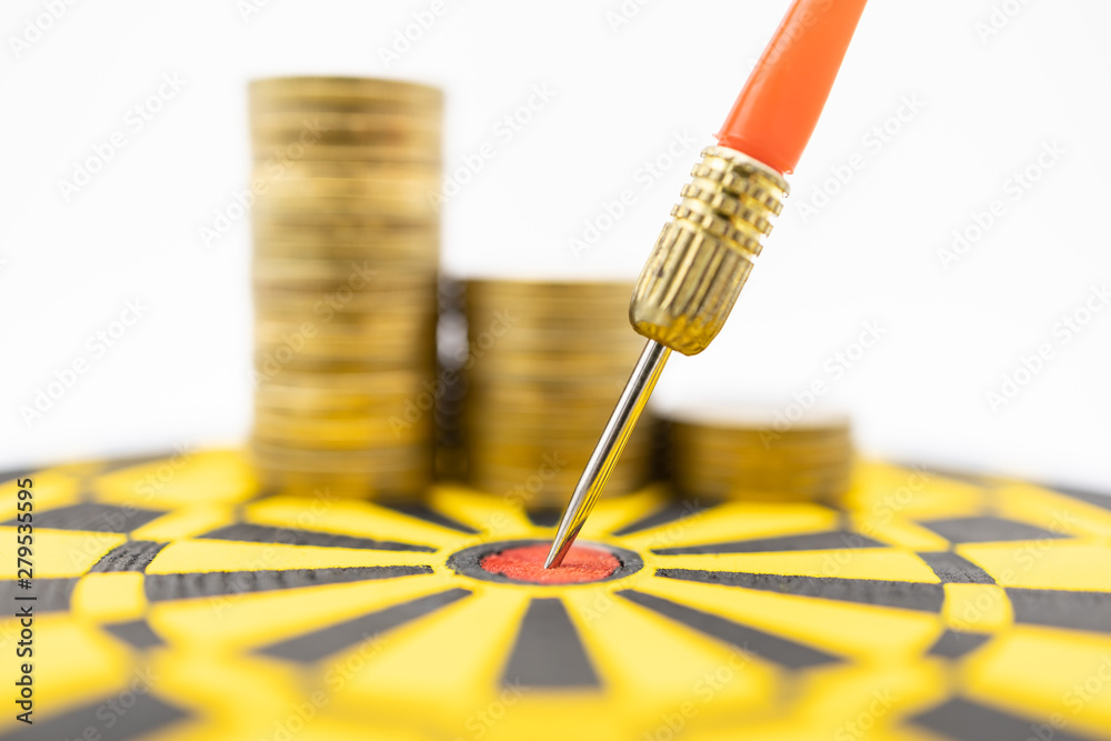 Money, Game, Business, Planning and Target Concept. Close up of dart stab on center of black and yellow board with stack of gold coins on white background. Money, Game, Business, Planning and Target Concept. Close up of dart stab on center of black and yellow board with stack of gold coins on white background.
