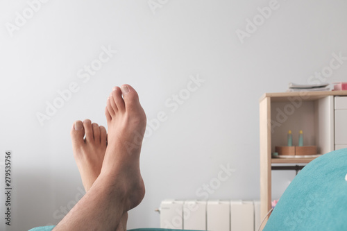 Two male feet relaxing on a green sofa on an indoor home scene