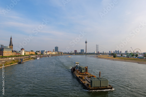 Barge or flat bottom ship on Rhein River and background of riverside and cityscape of city Düsseldorf in summer season against sunny blue sky. in Düsseldorf, Germany.