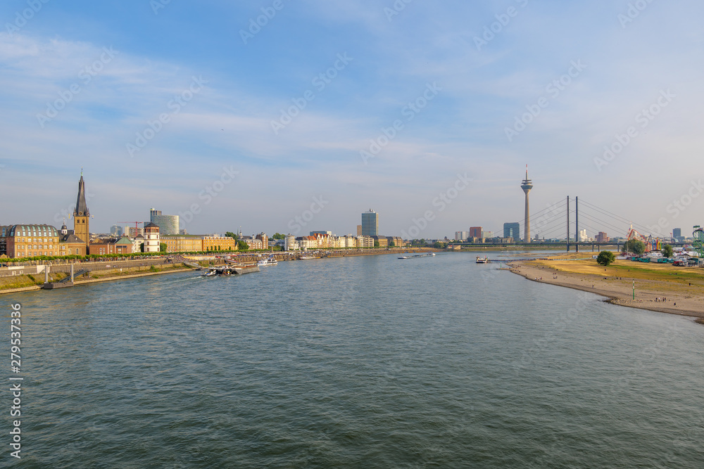 Outdoor panoramic sunny scenic cityscape view of Düsseldorf city, Germany, with promenade walkway on waterfront through old town and downtown, view from the bridge over Rhine River. 