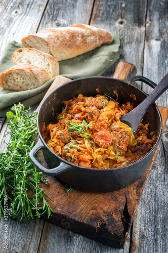 Traditional Polish kraut stew bigos with sausage, meat and mushrooms as closeup in a cast iron pot on an old wooden table photo