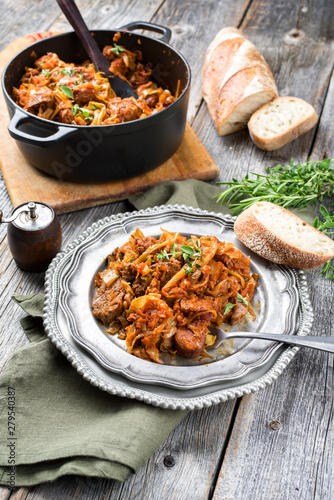 Traditional Polish kraut stew bigos with sausage, meat and mushrooms as top view in a cast iron pot and pewter plate on an old rustic board photo