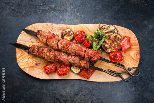 Traditional Russian shashlik on a barbecue skewer with vegetable and sumach as top view on a wooden cutting board with copy space