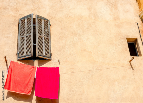 Red towels on clothes line against yellow wall of house with window