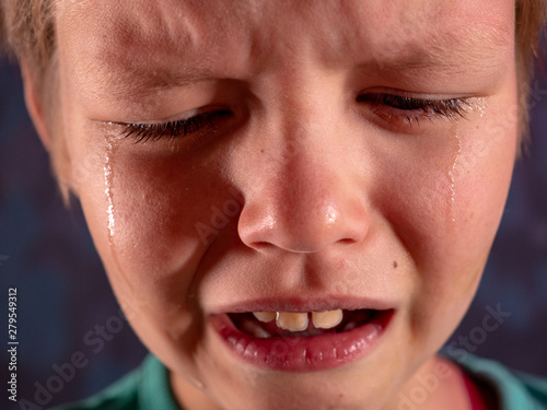 Face of crying boy close up. Eyes, eyelashes, eyebrows, lips, teeth and tears. Emotions and grimaces of upset child