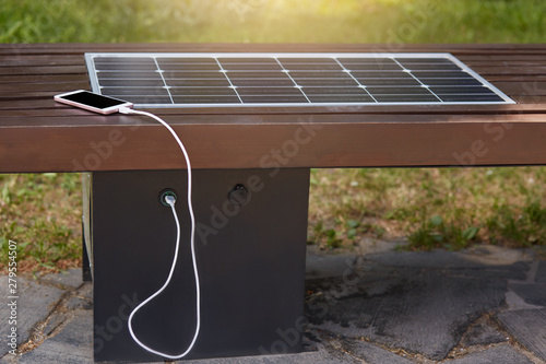 Close up outdoor image of smartphone charging via USB in park with help of solar panel installed inside wooden bench. Modern technologies, alternative sources of energy. Environment concept. photo