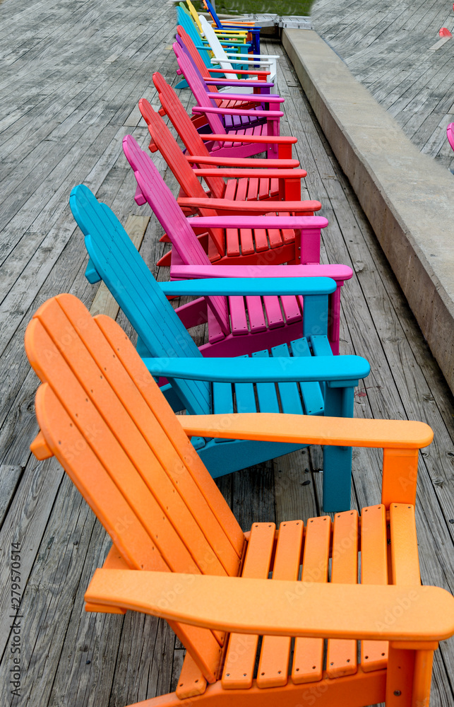 Colorful Wood Adirondack Chairs Lined Up on a Dock Overlooking a River Colorful Wood Adirondack Chairs Lined Up on a Dock Overlooking a River
