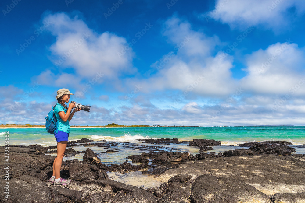 Ecotourism tourist photographer taking wildlife and landscape photos on Galapagos Islands. Woman photographer taking pictures on Isabela island in Puerto Villamil Beach. Marine Iguanas.