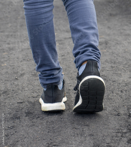 A boy with blue jeans and black sneaker shoes in black path