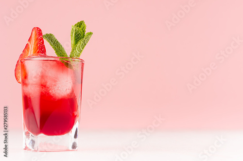 Red sweet cold party drink in elegant shot glass with ice cubes, strawberry slice, green mint on pastel soft pink color background, white wood board. photo