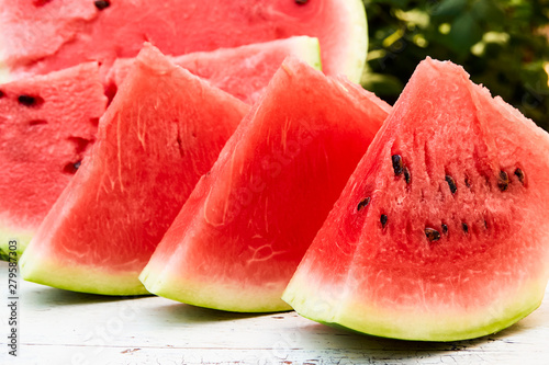 Fresh ripe striped sliced watermelon on a wooden old table, against the background of green leaves, outdoors.