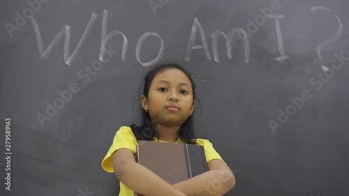 Female elementary school student standing in the class while holding a book with text of Who Am I? photo