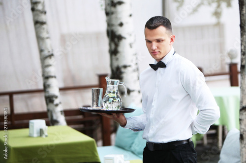 A young, handsome waiter is holding a tray in a carafe of water. The concept of the restaurant business. The staff in the field of restaurant business. photo
