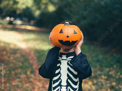 boy in a skeleton costume with a pumpkin on the holiday of Halloween