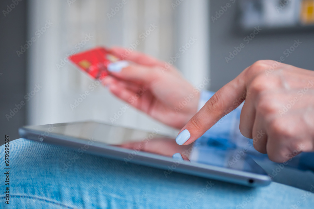 Fototapeta premium Woman using black digital tablet device and entering security code of red credit card. Online shopping, buying, e-commerce, sale, consumerism, internet shop, electronic payment, technology concept