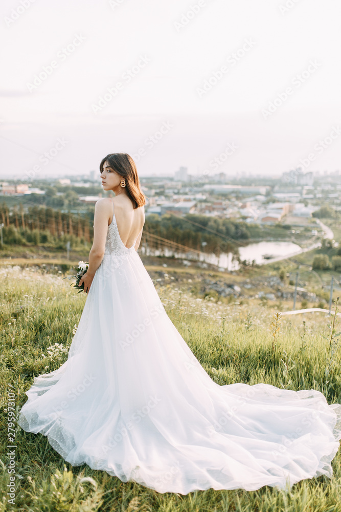 Bride with long dress in nature with sunset. A stylish wedding in the European style of fine art.