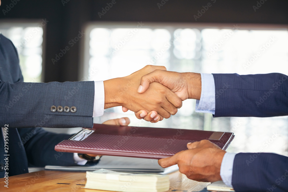 Obraz premium Young business people shaking hands in the office. Finishing successful meeting. Businessman holding pens and holding graph paper are meeting to plan sales to meet targets set in next year.