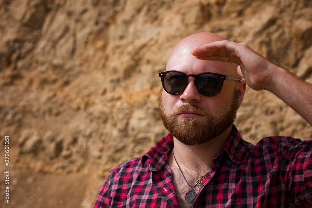 brutal man in glasses and a hat on the background of rocks brutal man in glasses and a hat on the background of rocks