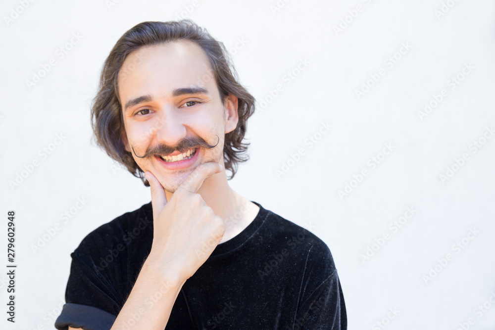 Happy young man with handlebar mustache looking at camera. Closeup shot of stylish young guy holding hand on chin. Happiness concept Happy young man with handlebar mustache looking at camera. Closeup shot of stylish young guy holding hand on chin. Happiness concept