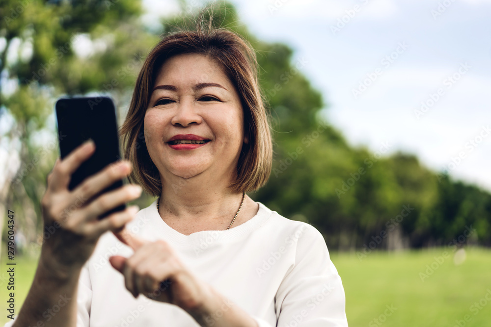 Portrait of happy senior adult elderly asia women smiling and using and talking on the phone in the park.Retirement concept Portrait of happy senior adult elderly asia women smiling and using and talking on the phone in the park.Retirement concept