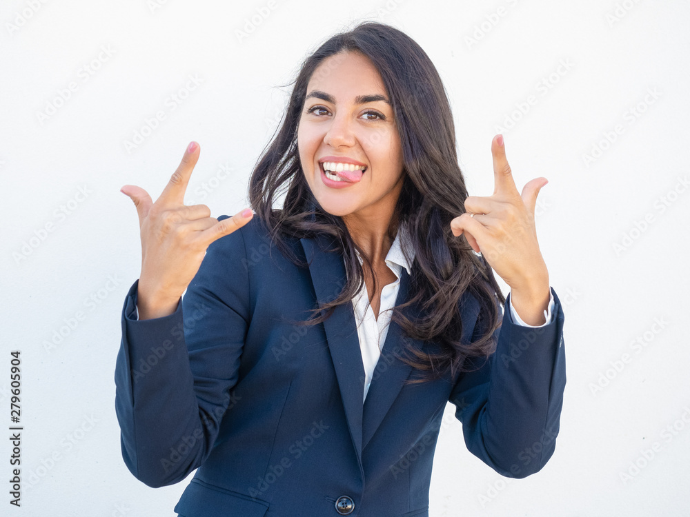 Cheerful funny businesswoman showing heavy metal sign. Happy smiling beautiful young Latin woman in office suit making hand rock gesture, sticking out her tongue. Heavy concept Cheerful funny businesswoman showing heavy metal sign. Happy smiling beautiful young Latin woman in office suit making hand rock gesture, sticking out her tongue. Heavy concept