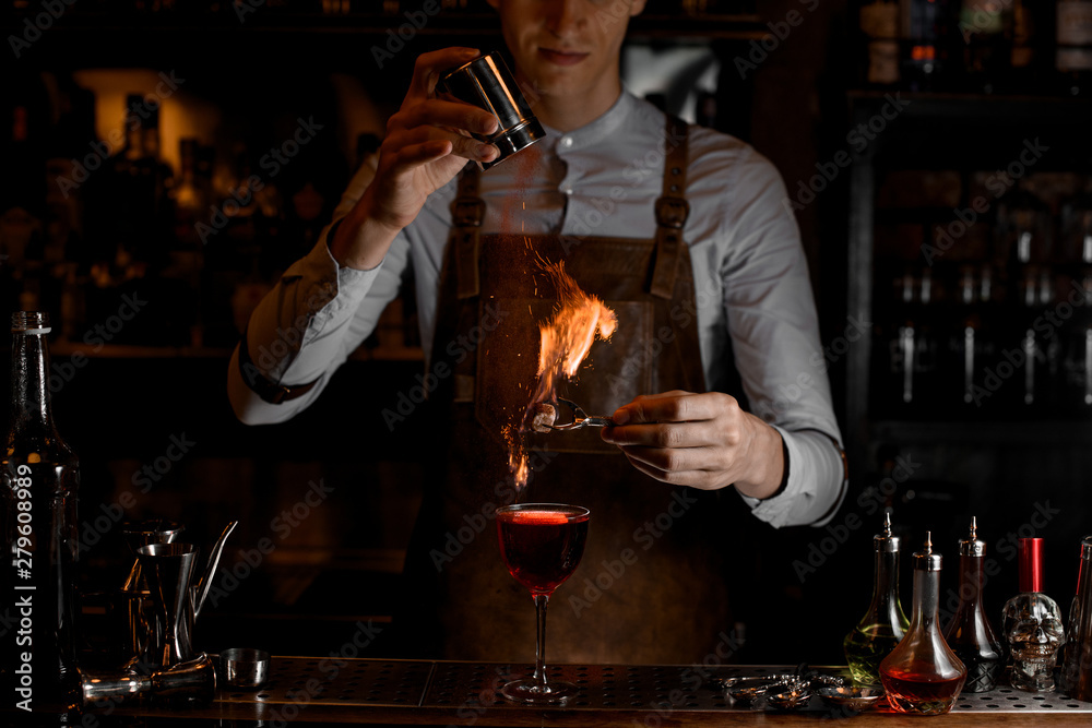 Bartender add spices for a decor in the fire above a delicious red cocktail in the glass