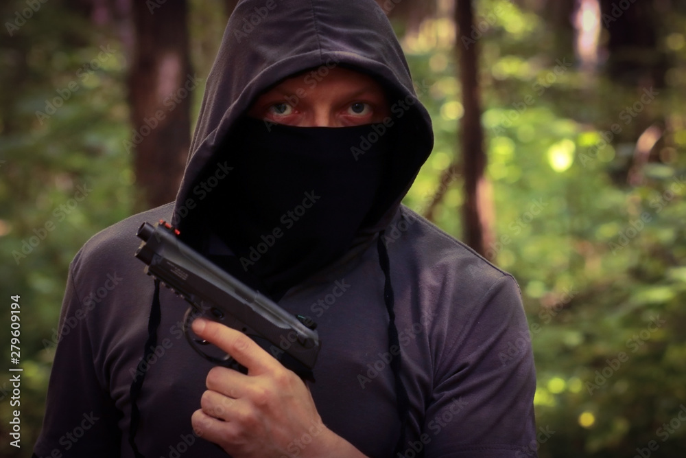 Man in hood with the pistol in the forest. Man in hood with the pistol in the forest.