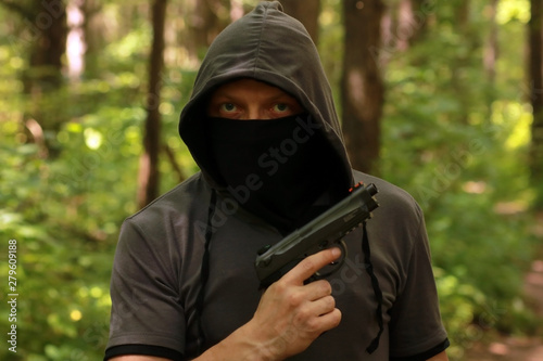 Man in hood with the pistol in the forest.