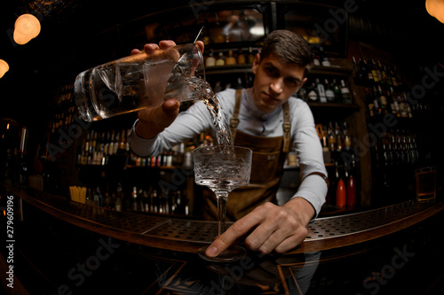 Fisheye shot professional male bartender pouring a cocktail from the measuring cup to the glass