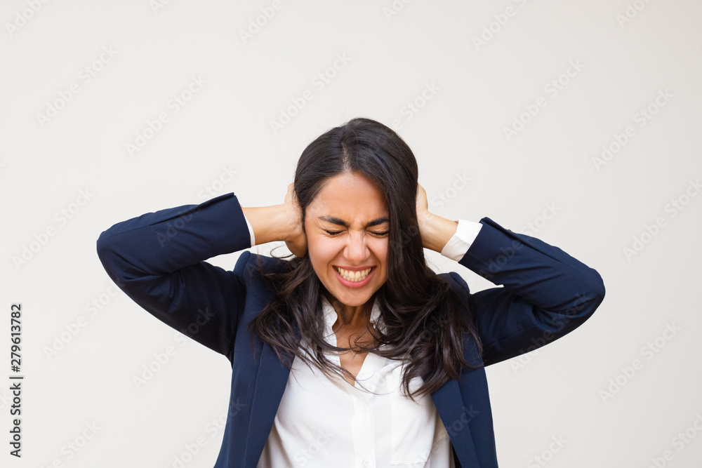 Young businesswoman closing ears. Stressed young woman in formal wear standing with closed eyes and closing ears isolated on grey background. Emotion concept Young businesswoman closing ears. Stressed young woman in formal wear standing with closed eyes and closing ears isolated on grey background. Emotion concept