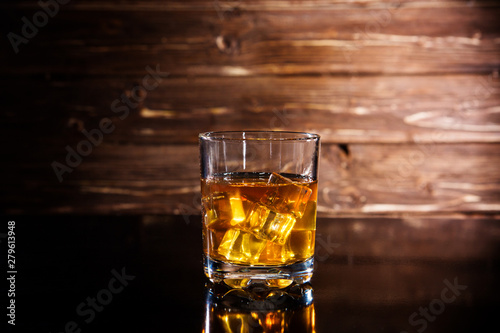 Glasss of whiskey with ice cubes on wooden background