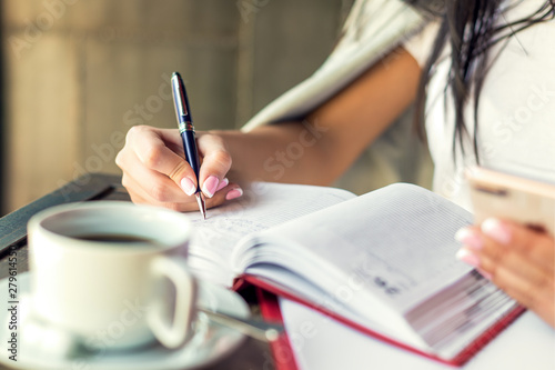 Young woman right hand writing plans on small diary in cafe close up