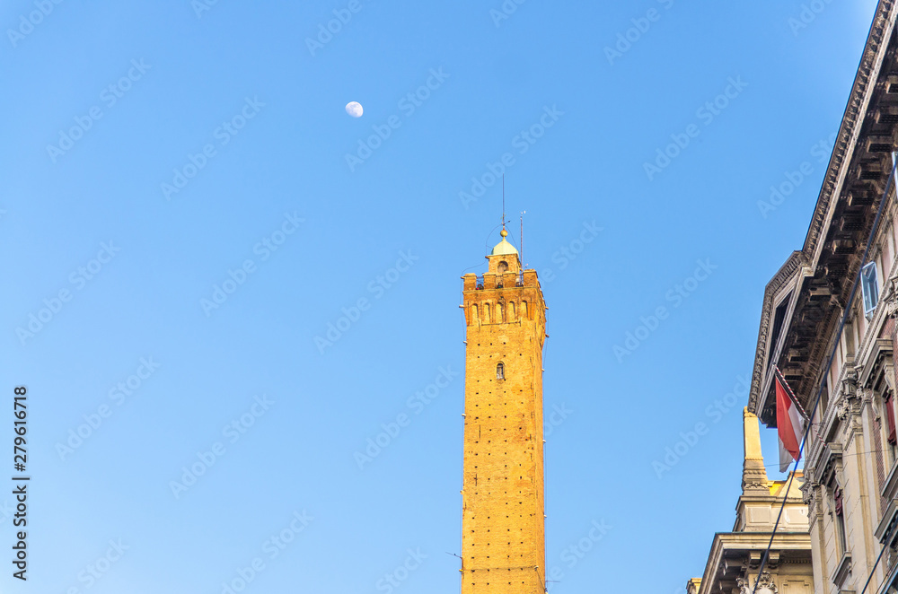 Obraz premium Top of Garisenda medieval tower of Bologna and moon with blue sky background in early evening, Emilia-Romagna, Italy