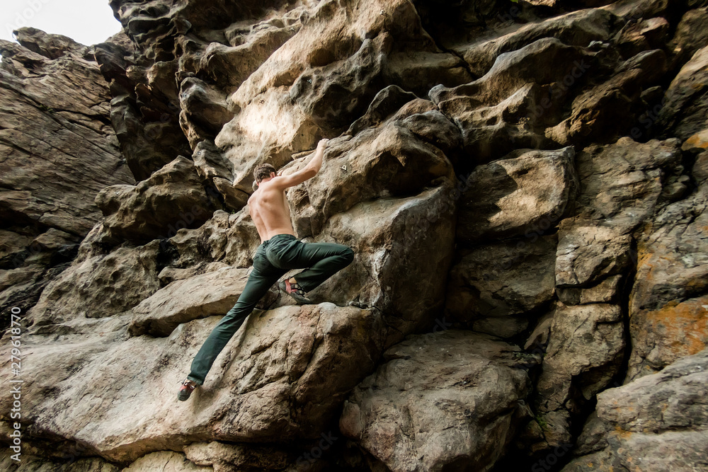 Rock climber climbs bouldering on a cliff on forest. Low angle of strong rock climbing man hanging free on rock with sunflare Rock climber climbs bouldering on a cliff on forest. Low angle of strong rock climbing man hanging free on rock with sunflare