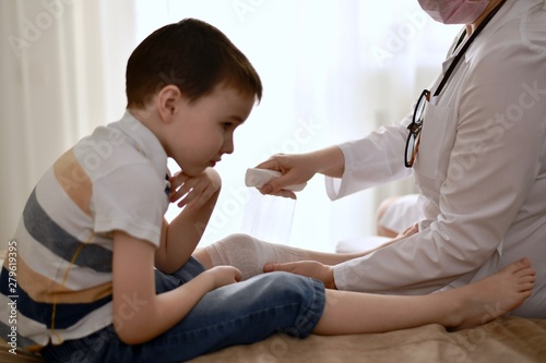The hands of the doctor carefully bandage the knee of the child who is distressed from the injury.