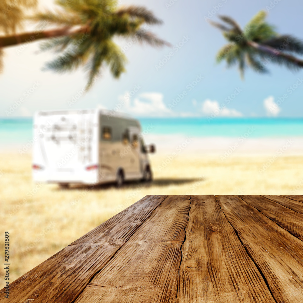 Obraz premium Table background with wooden board in the beautiful ocean and beach view. Palm leaves and clear sunny sky. Free space on a wooden table for an advertising product.