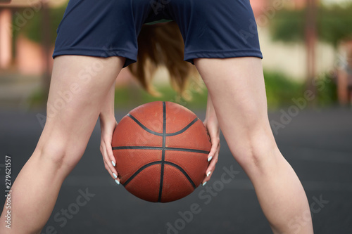 Caucasian girl holding ball between legs during a street basketball game at outdoor court